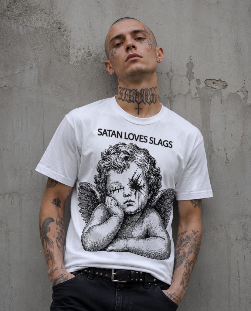 White T-shirt printed with a distressed black cherub graphic, scratched-out eyes and the words “SATAN LOVES SLAGS” in red and black lettering.